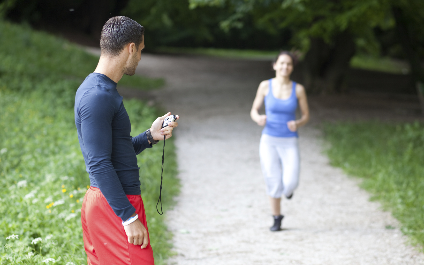 Personal trainer timing a female runner. Selective focus.