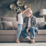 Profile photo of funny aged old grandpa golden crown head little pretty granddaughter playing famous people roles stay home quarantine safety modern interior living room indoors